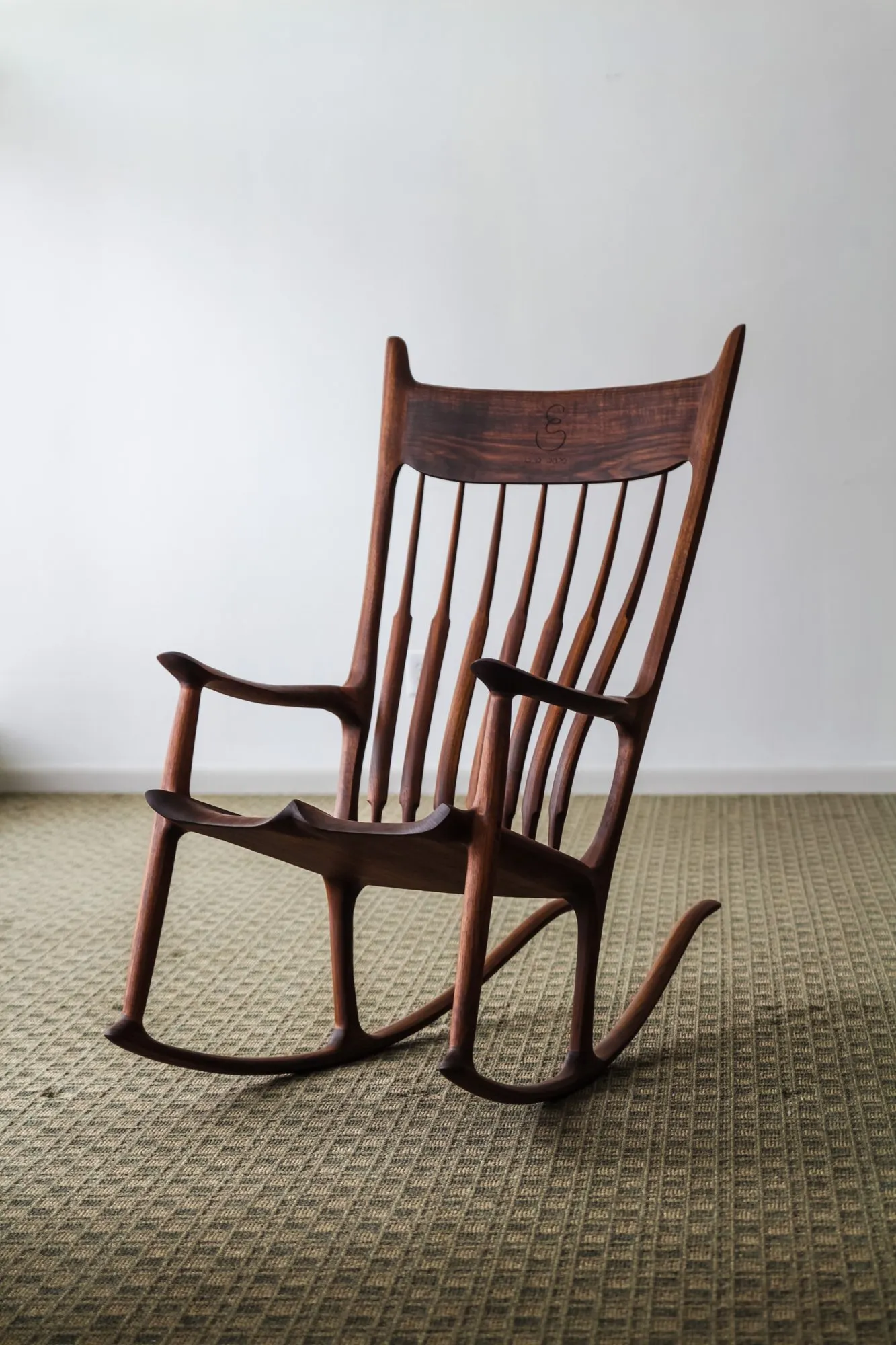 The full rocking chair seen from the front three-quarter view, showing the fanned spindle back, sculpted arms, shaped seat, and curved runners.
