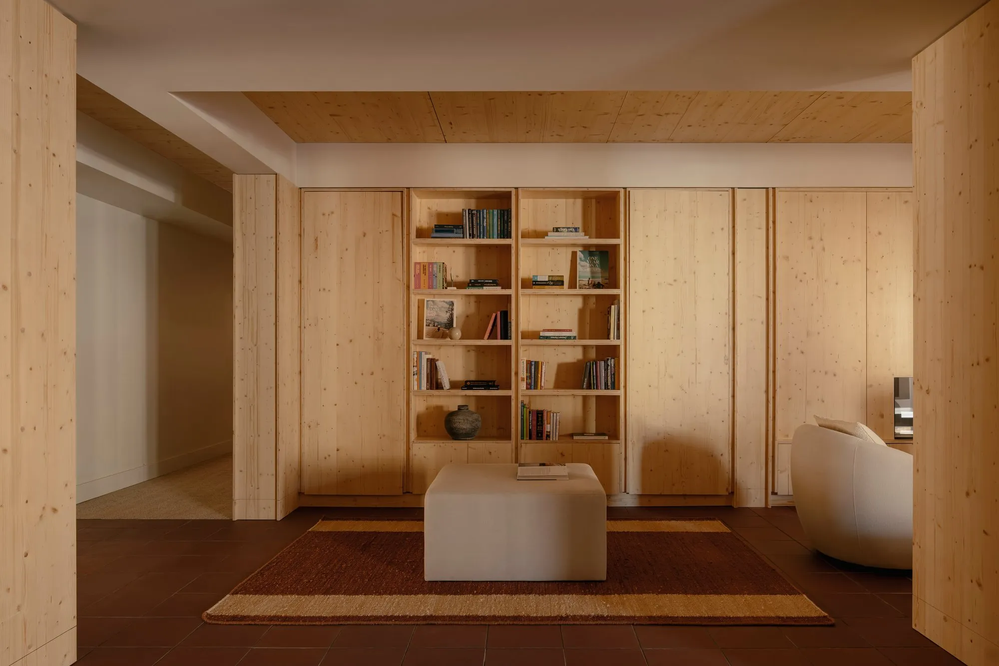 A full-height pine bookshelf built into a wall of pine panelling in the living area, flanked by concealed door panels.