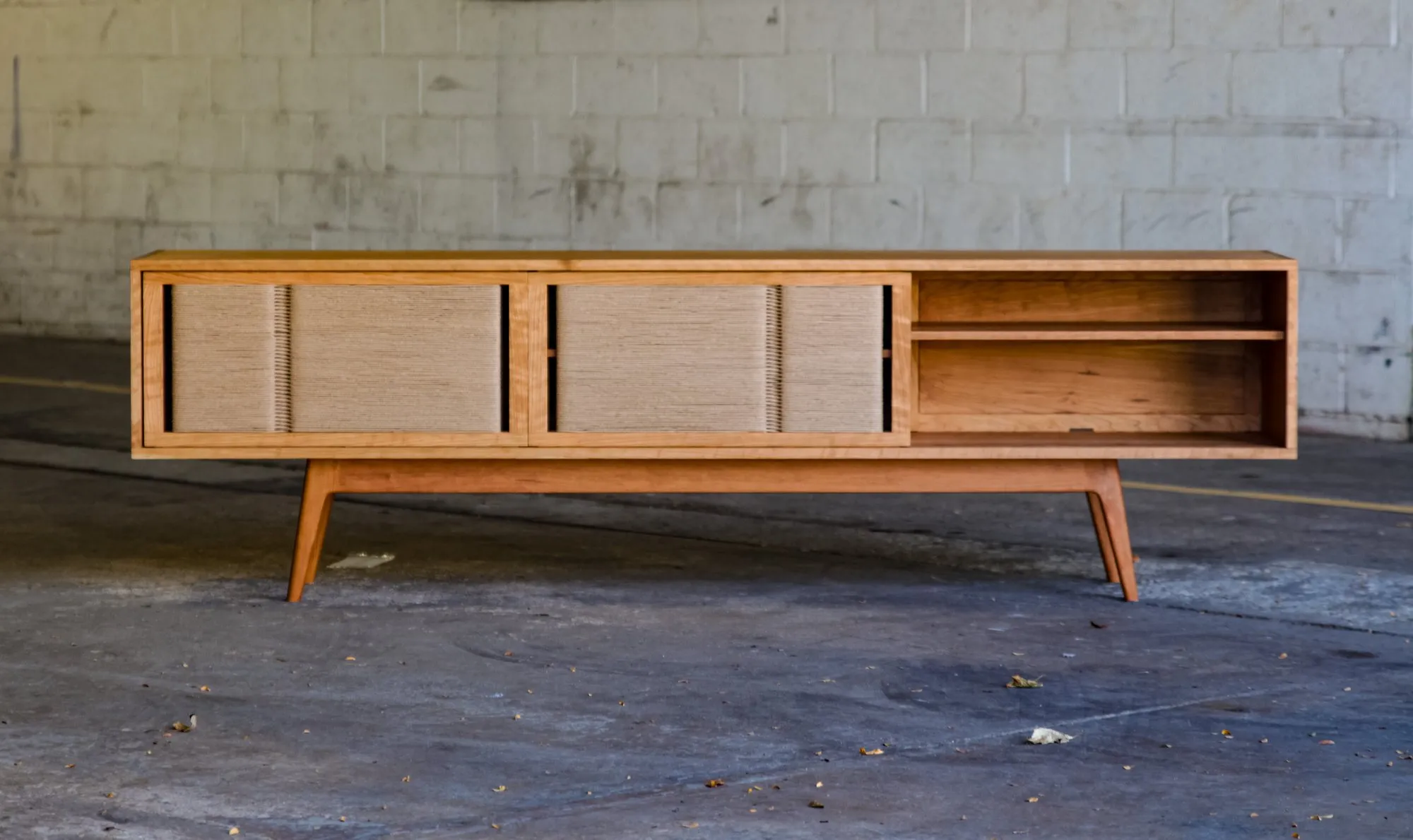 The credenza with both doors slid to the left, revealing an open shelved compartment on the right side of the case.