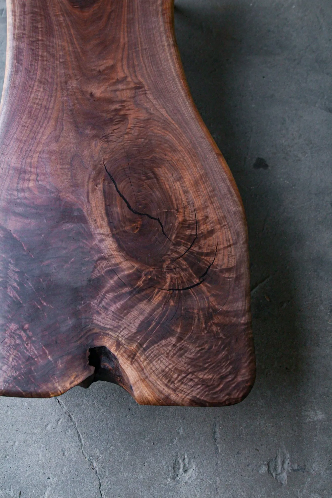 Top-down view of the walnut slab, showing swirling figured grain, a natural crack, and the undulating live edge.