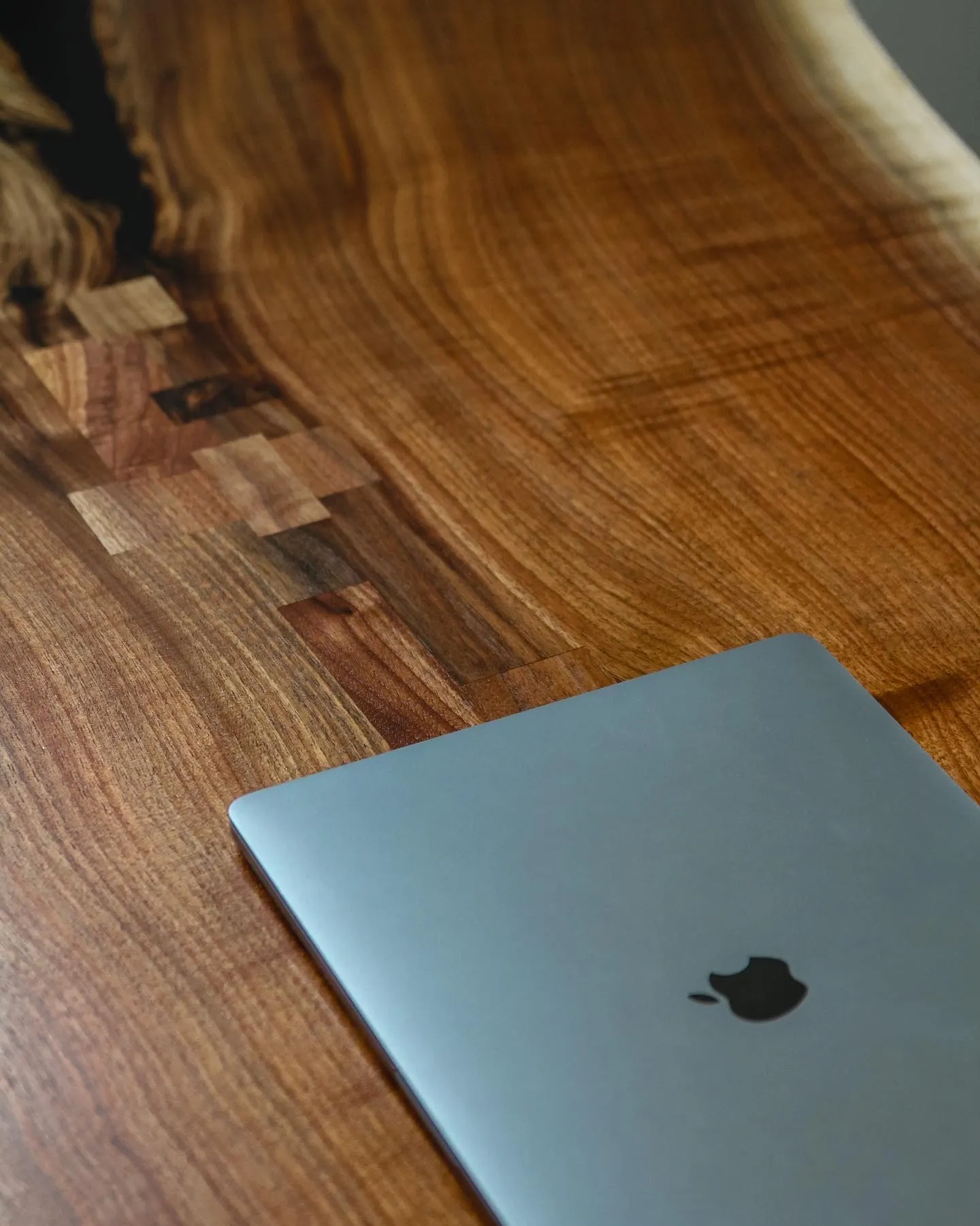 The figured walnut desktop in use, with a laptop resting on the pieced grain and a live edge running along the far side.