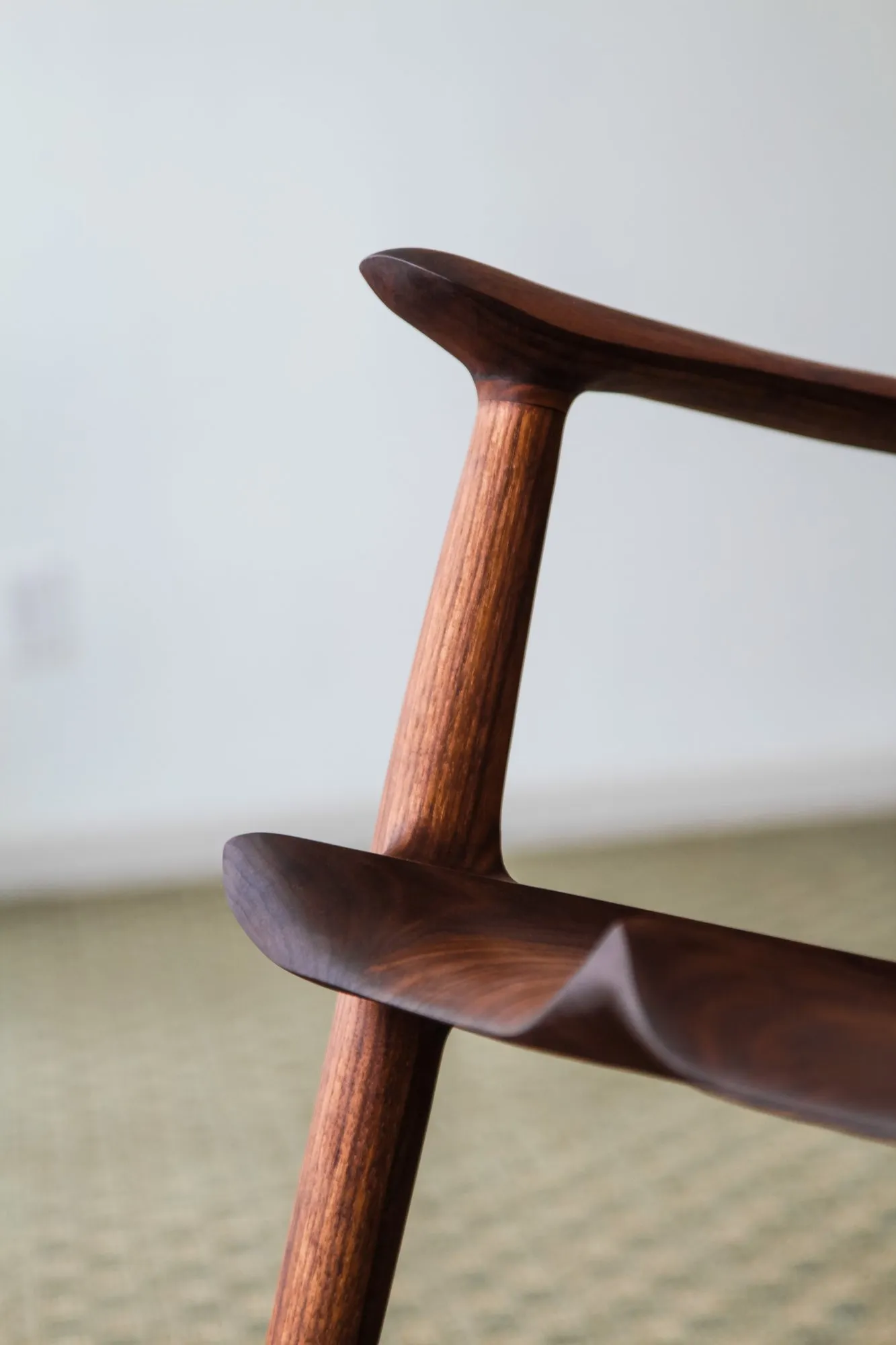 Close detail of the shaped walnut arm flowing into the front post, the surfaces carved into soft continuous curves.