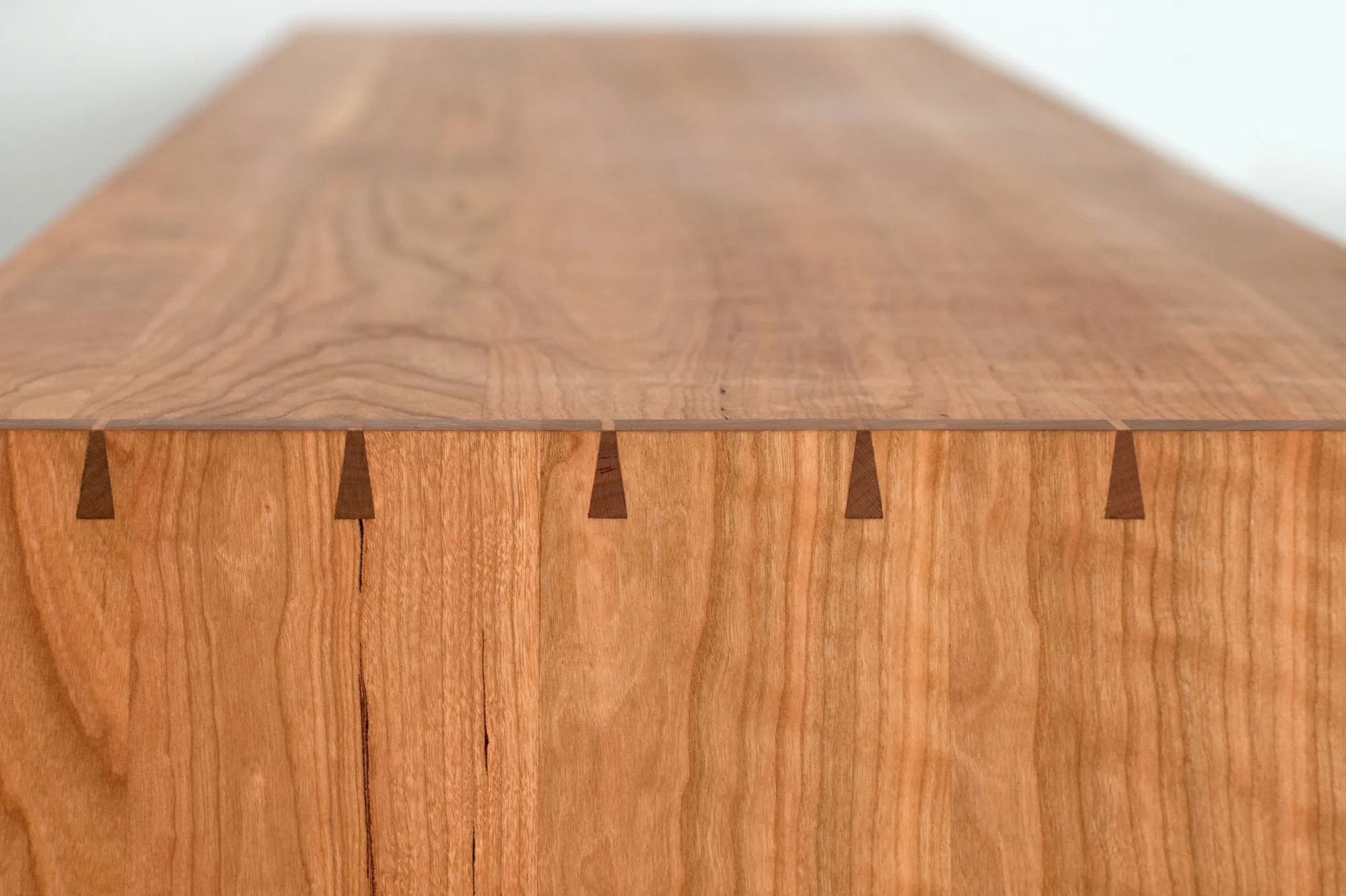 Close detail of the top corner showing hand-cut through-dovetails, with dark contrasting keys set into the lighter wood.