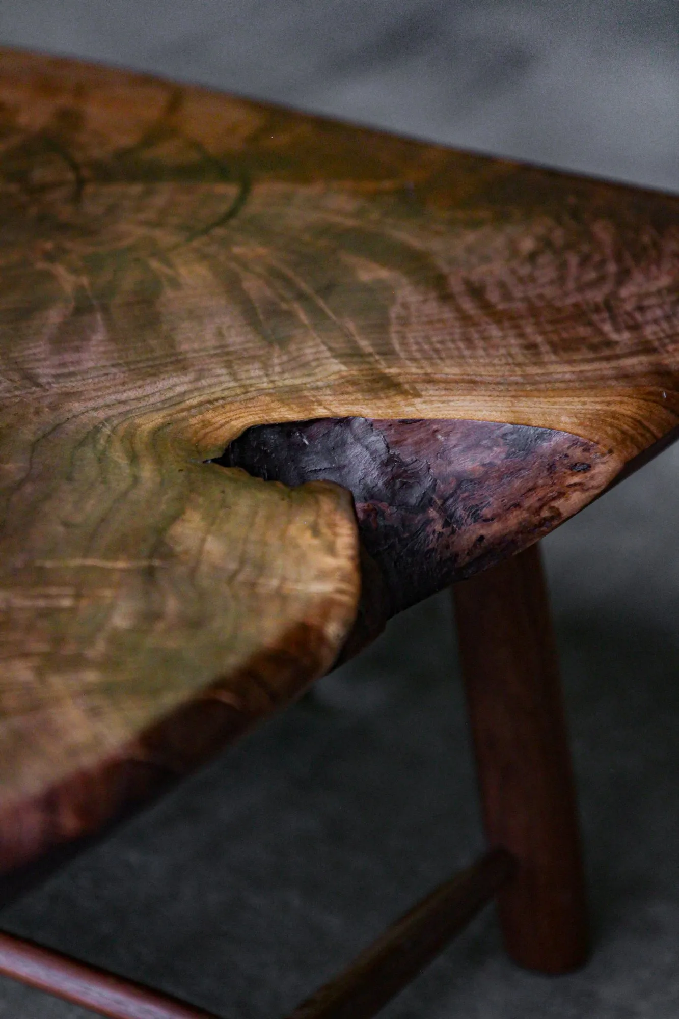 Close detail of the walnut slab where pale sapwood meets dark heartwood around a natural void in the grain.
