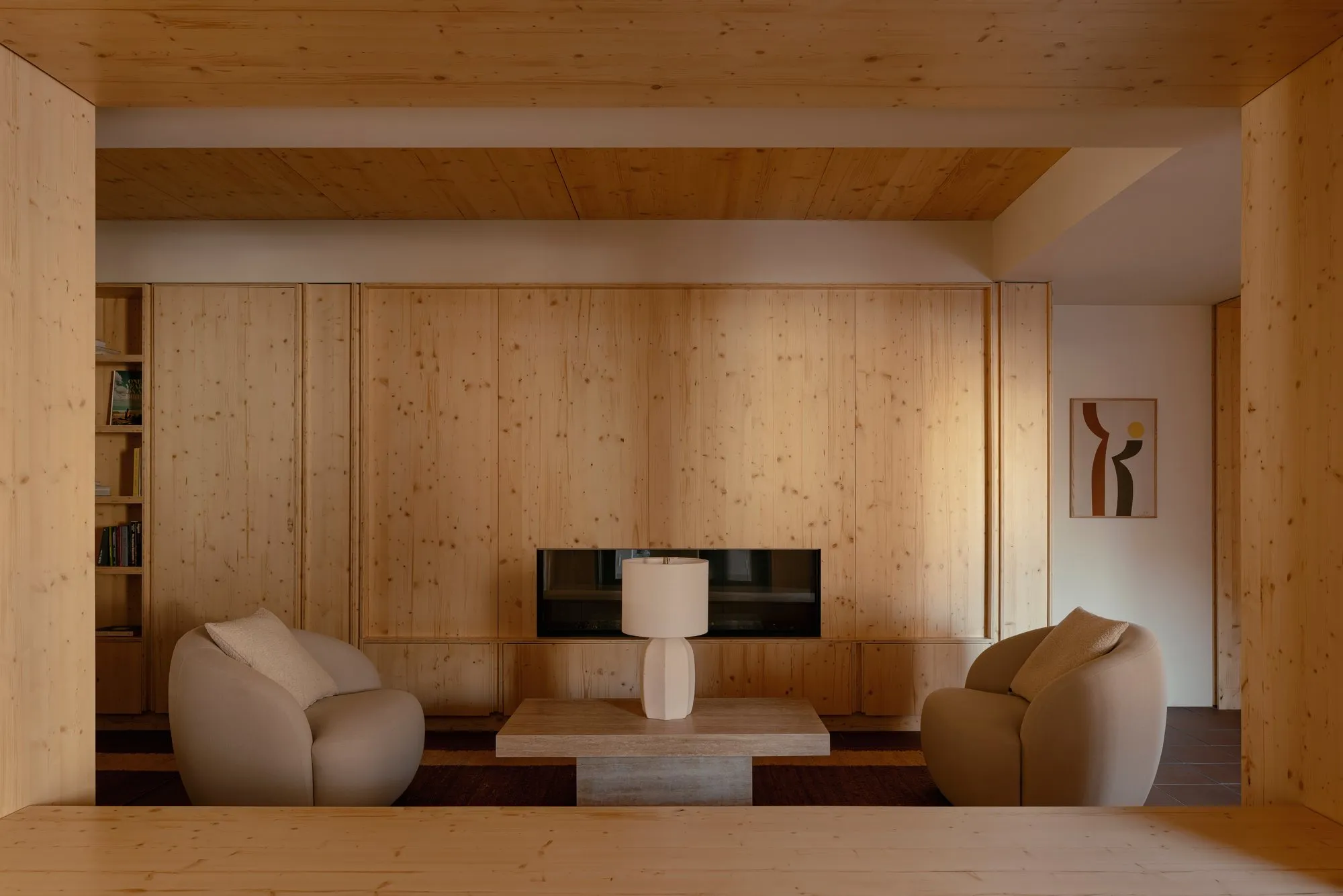 A pine-panelled living room wall with a media niche set into it, framed by two armchairs and a low stone table.