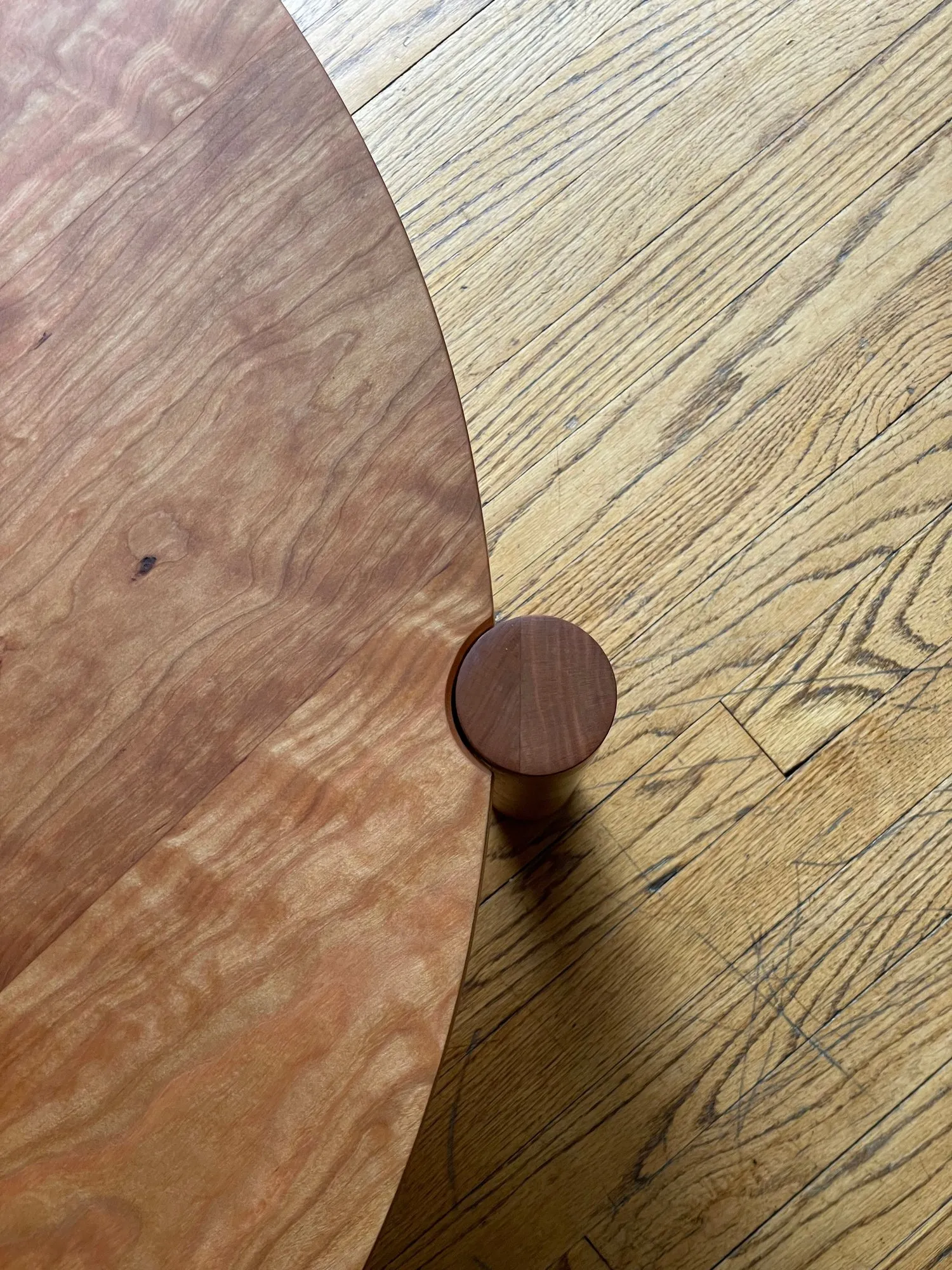 Overhead detail of the table edge where a round leg tenon shows through the top as a small darker circle set into the lighter cherry surface.