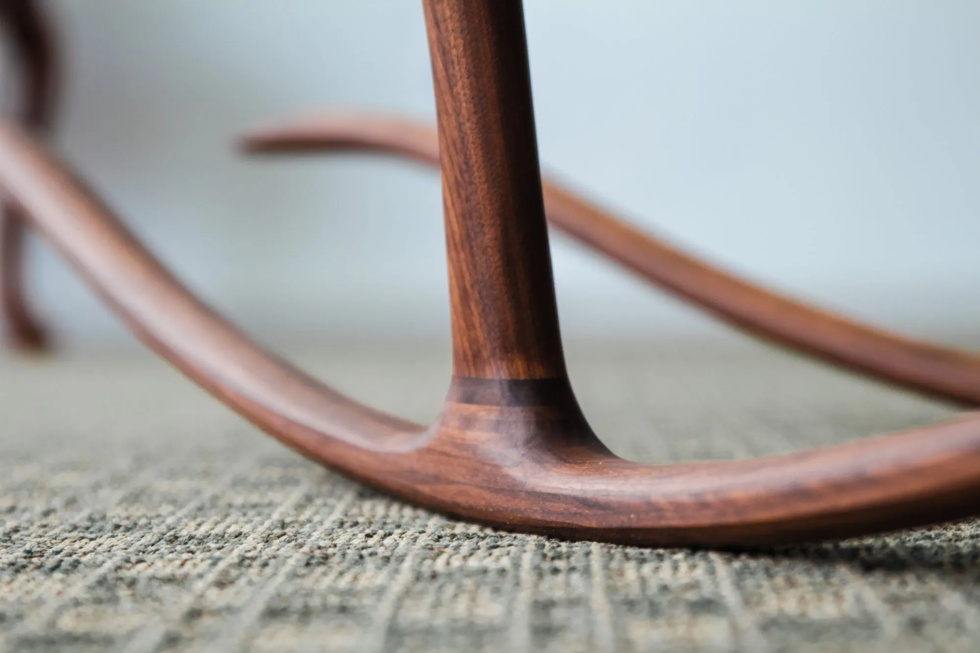 Detail of the leg meeting the long curved rocker, with two round contrasting joinery pins set into the walnut above the junction.