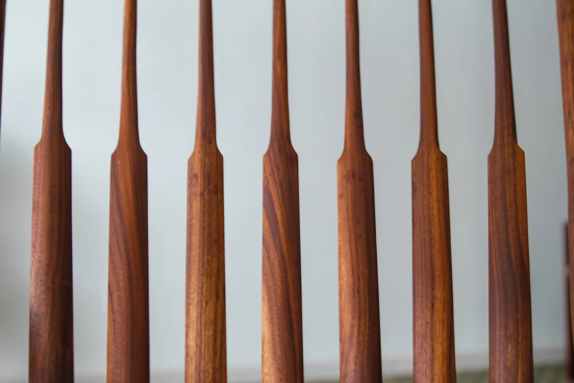 Close view of the tapered walnut spindles of the chair back, each shaped to a slim waist and lined up in a row.