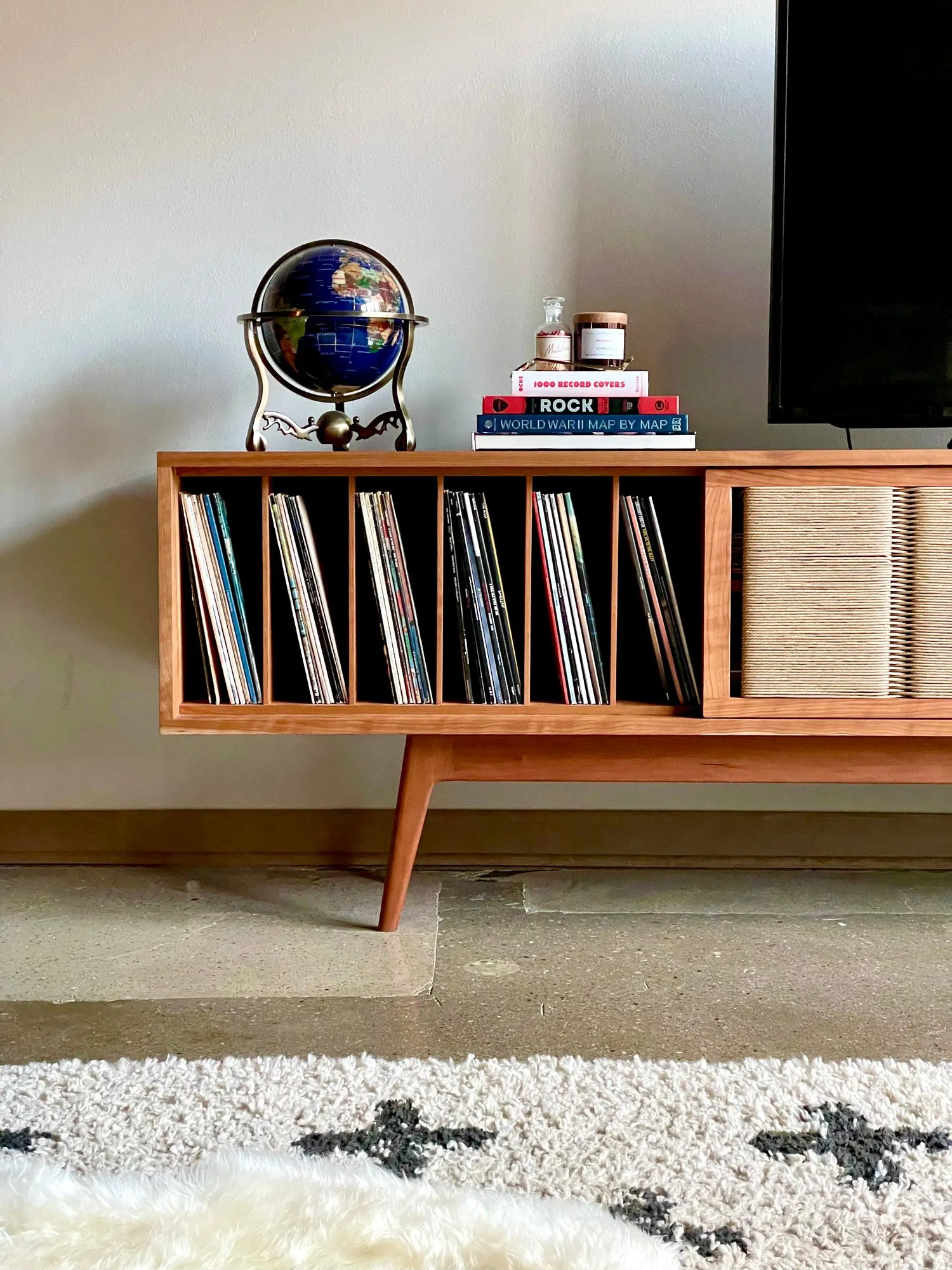 The Arnold Credenza in a room, holding a row of vinyl records behind an open door, with a globe and stacked books on top