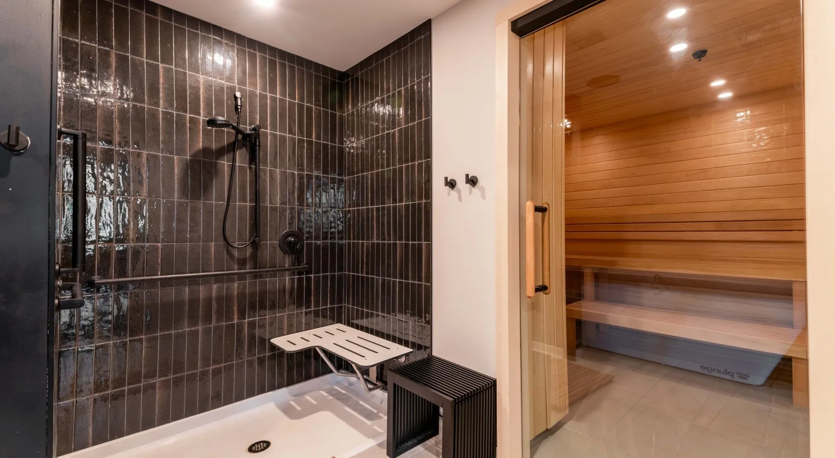 The wellness suite — a cedar-lined sauna beside a dark-tiled shower with a fold-down bench.