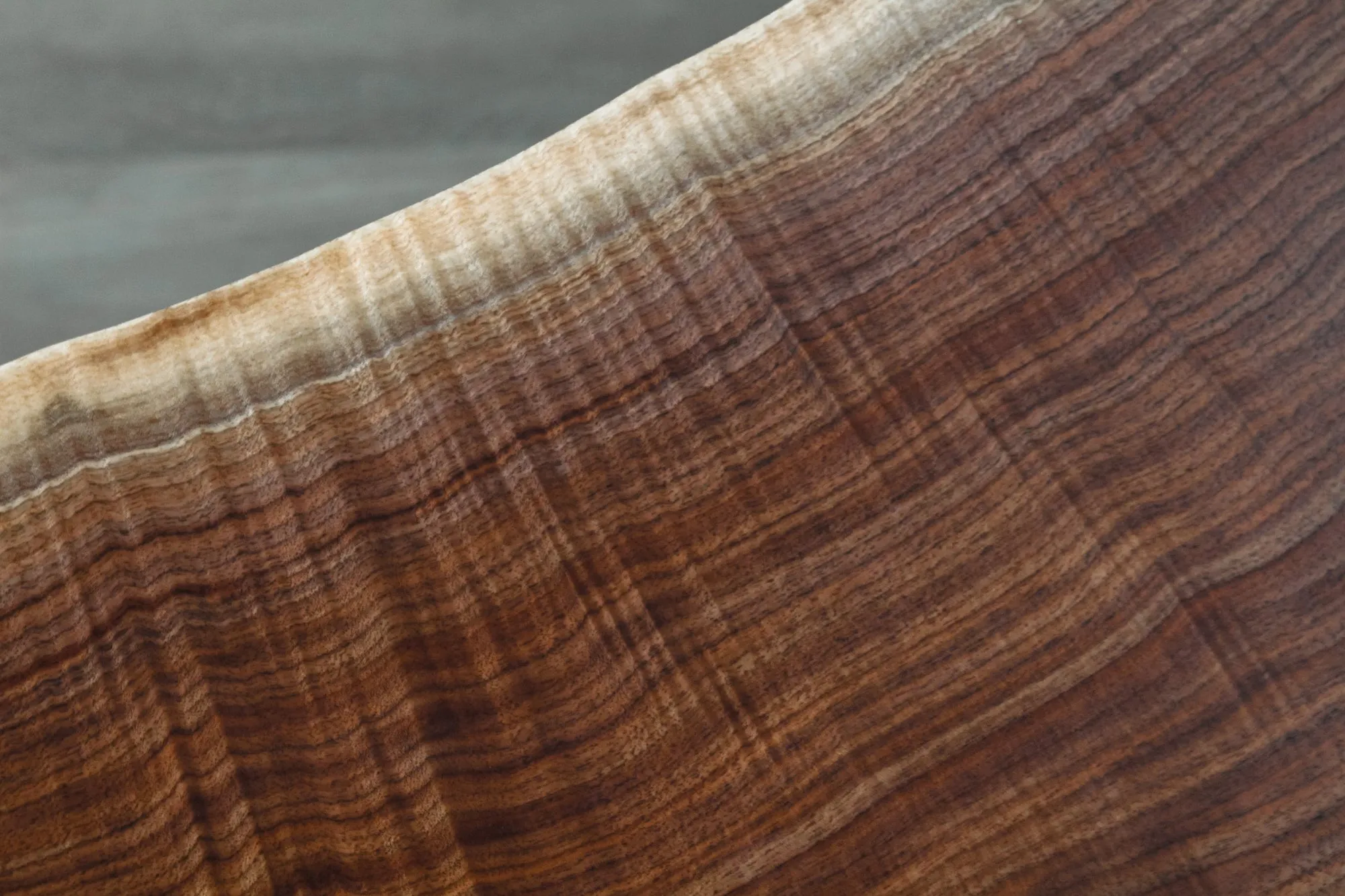 Close detail of the live edge of the walnut slab top, the dark heartwood fading to pale sapwood along the natural edge.